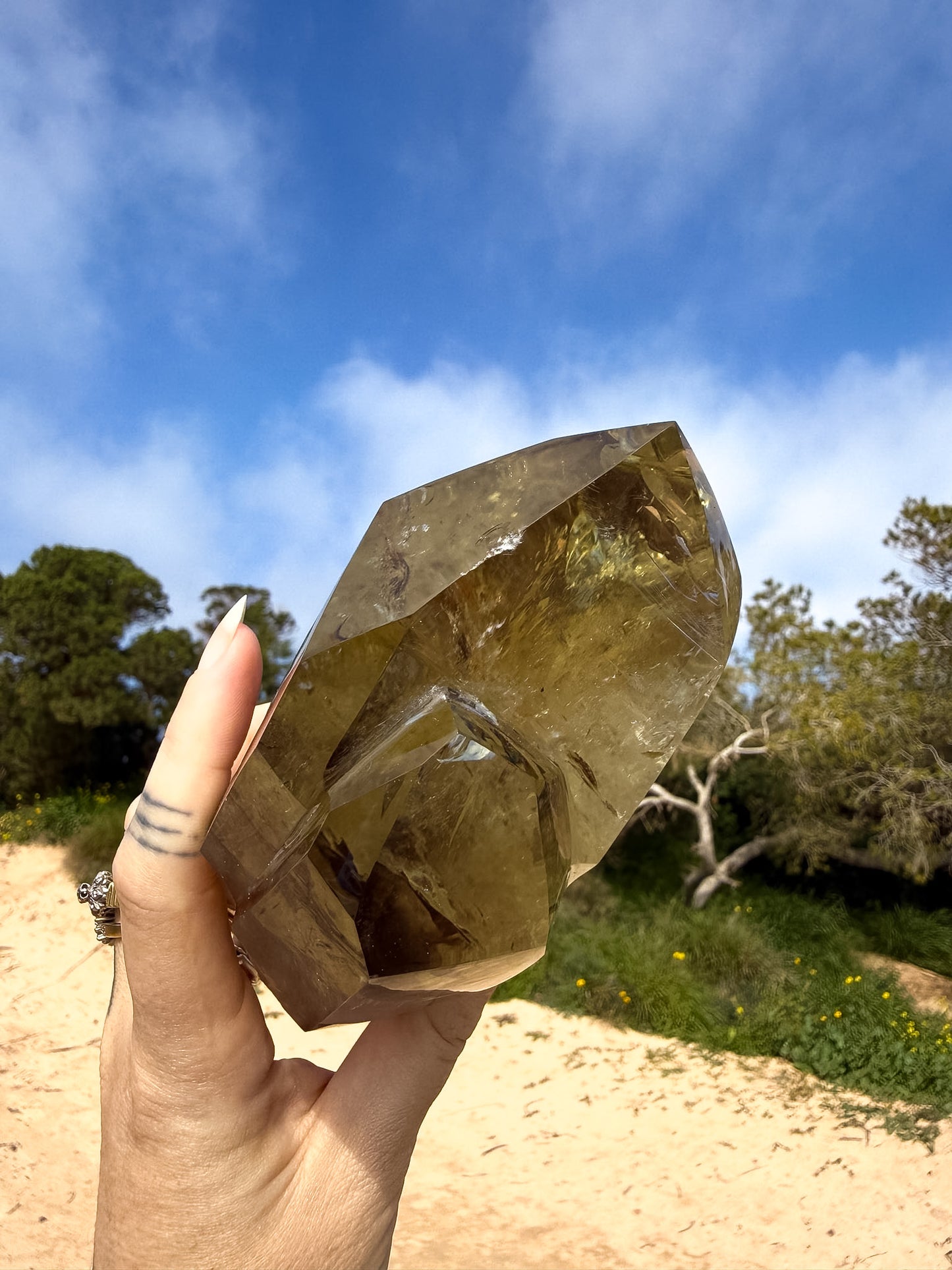 Hand holding large golden brazilian citrine double point with a natural background and blue sky