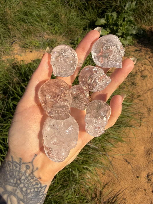 Hand holding clear quartz crystal skull-shaped carvings against a natural background