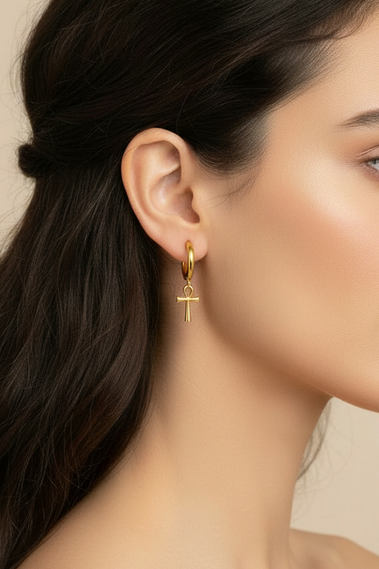 Gold hoop huggie earrings with sacred mini ankh pendants on a white background and on woman