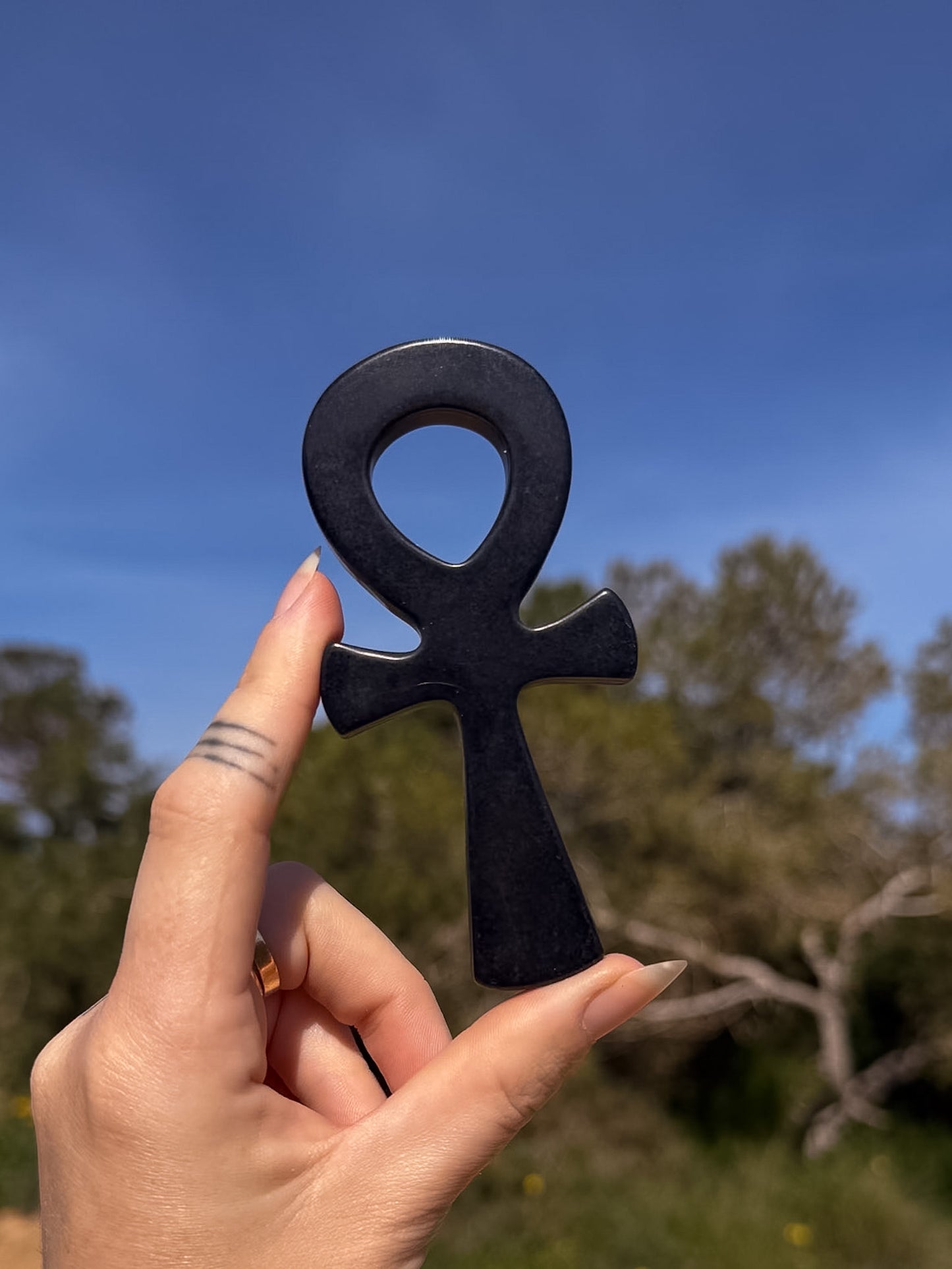 Obsidian crystal ankh carving held by a hand with a natural landscape background
