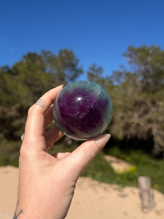 hand holding vibrant green and purple crystal sphere with green and sandy natural background