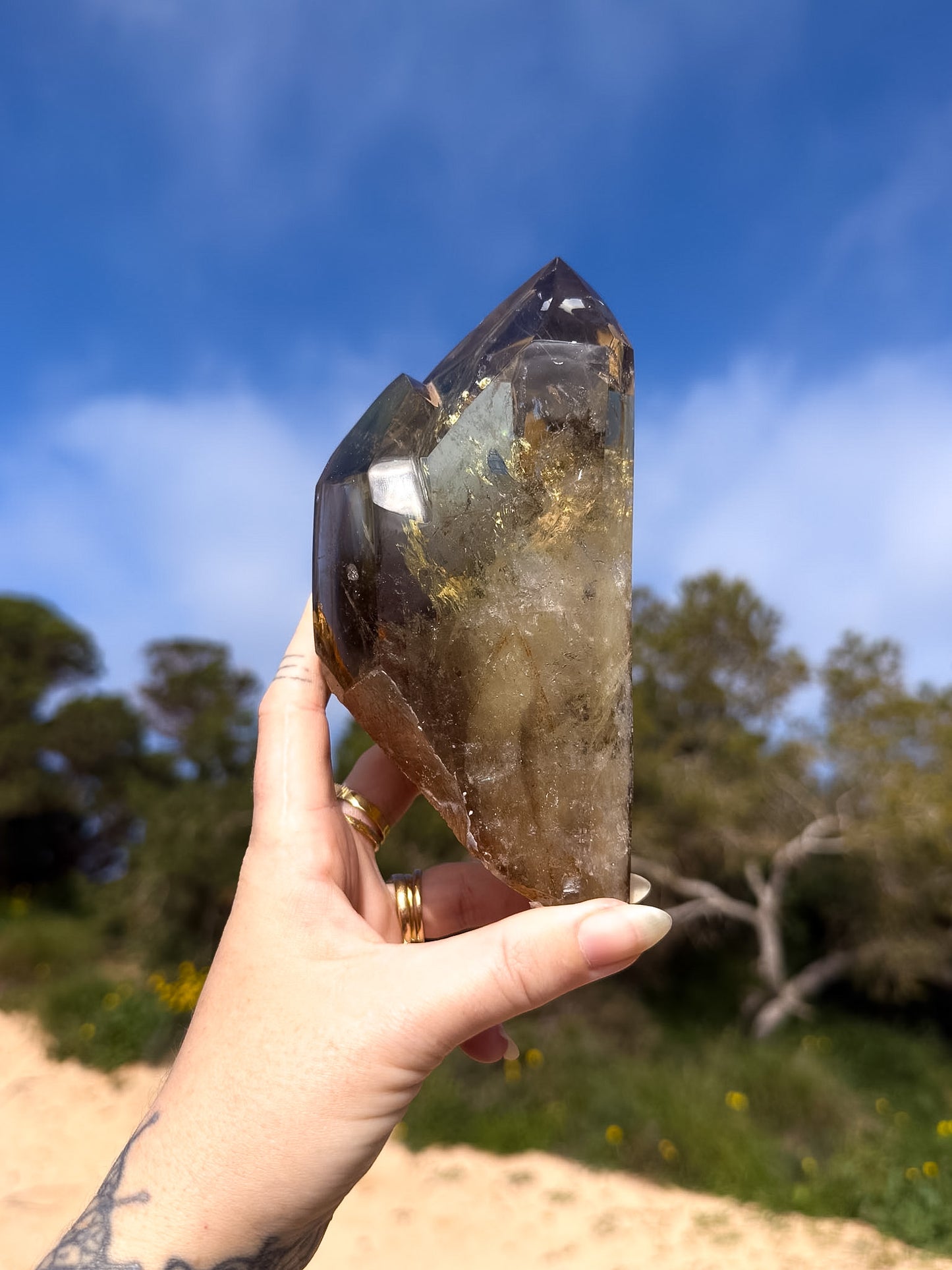 Hand holding large golden brazilian citrine double point with a natural background and blue sky 
