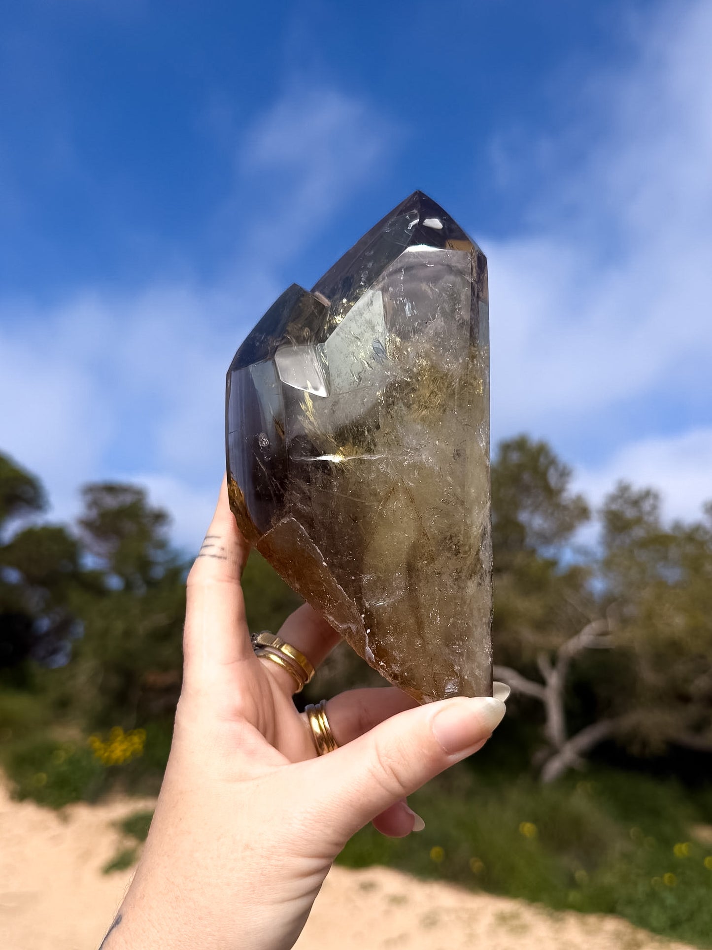 Hand holding large golden brazilian citrine double point with a natural background and blue sky 