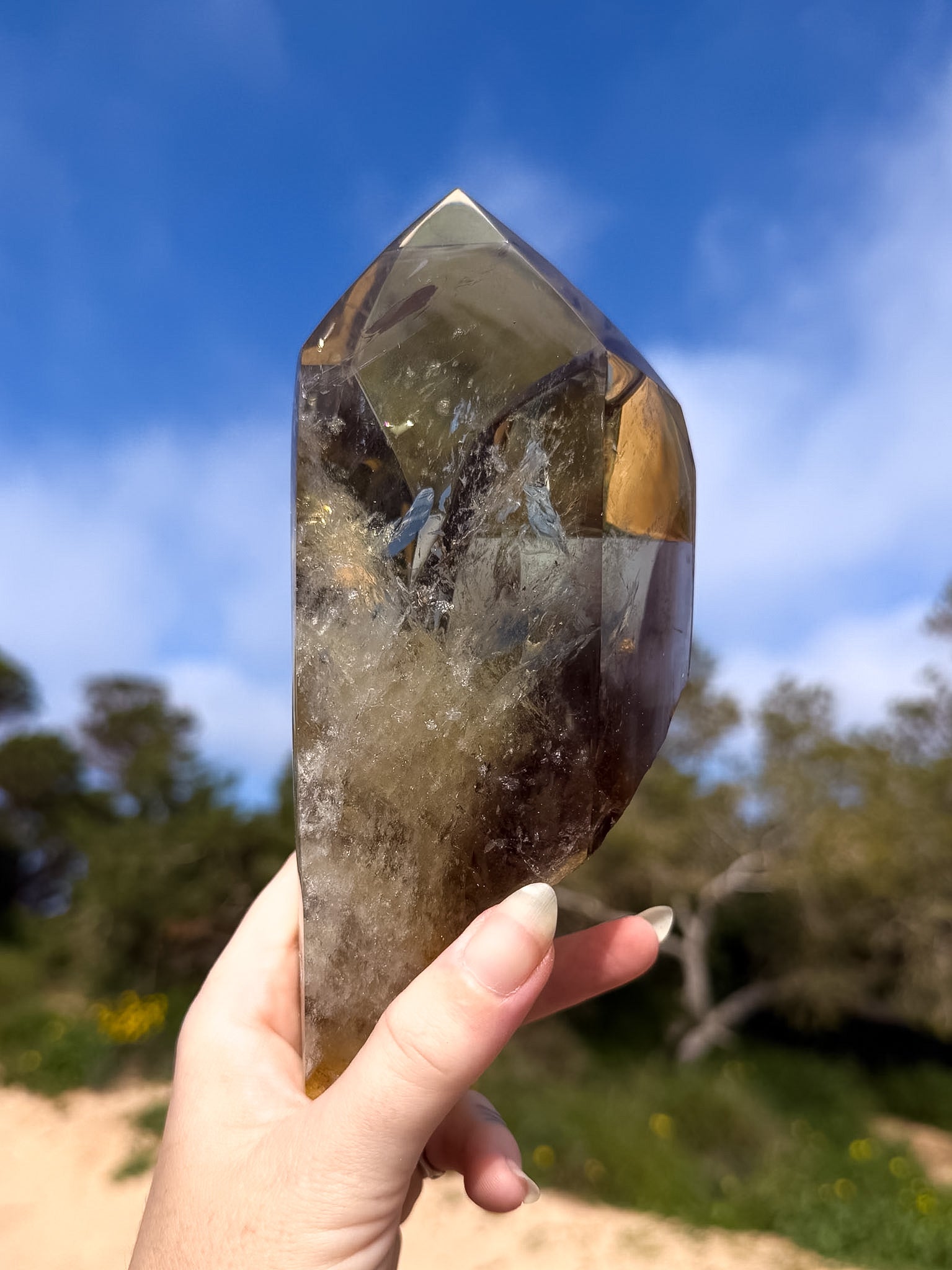 Hand holding large golden brazilian citrine point with a natural background and blue sky 