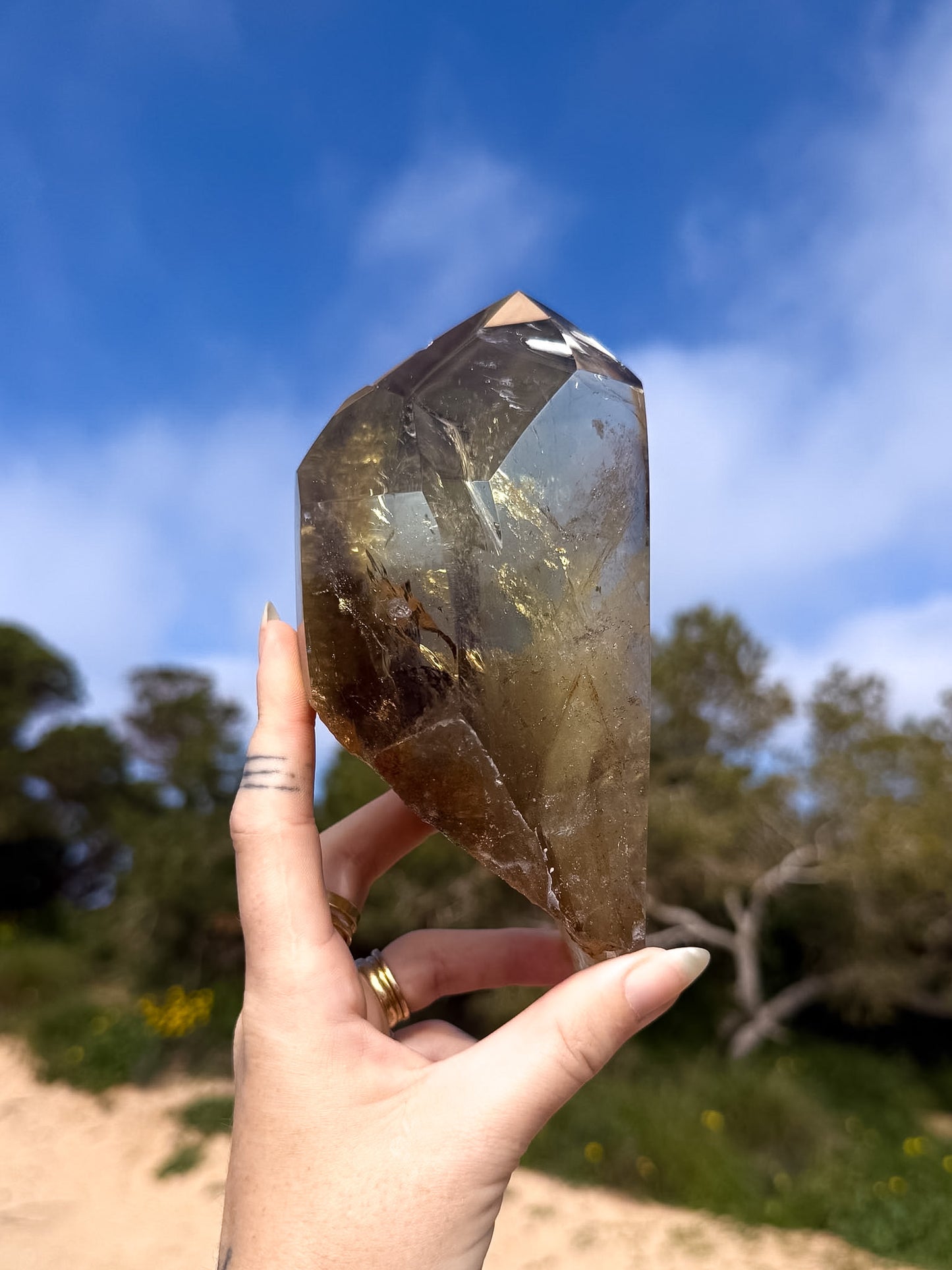 Hand holding large golden brazilian citrine point with a natural background and blue sky 
