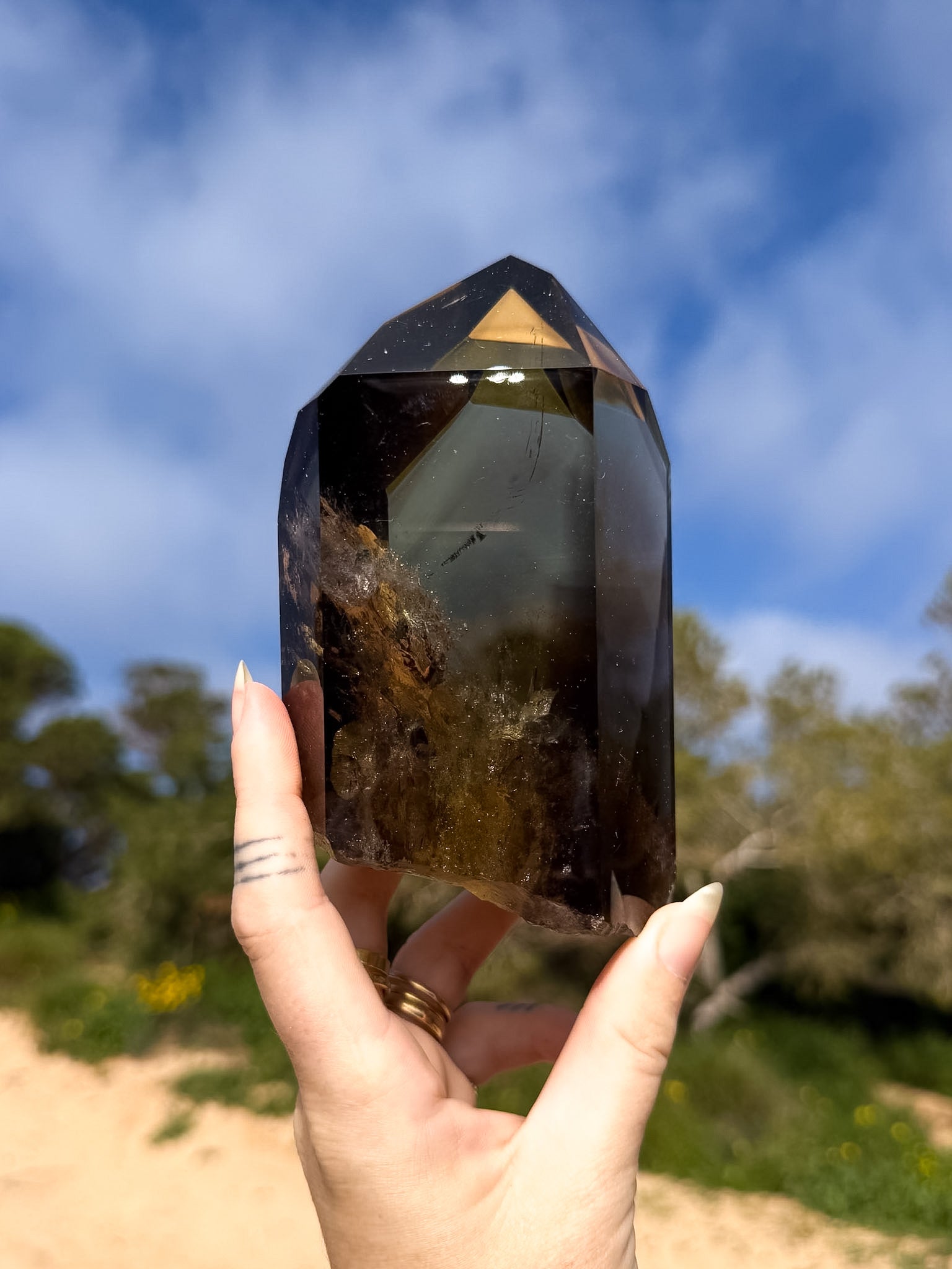 Hand holding large dark smoky brazilian citrine point with a natural background and blue sky 