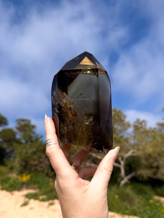 Hand holding large dark smoky brazilian citrine point with a natural background and blue sky 