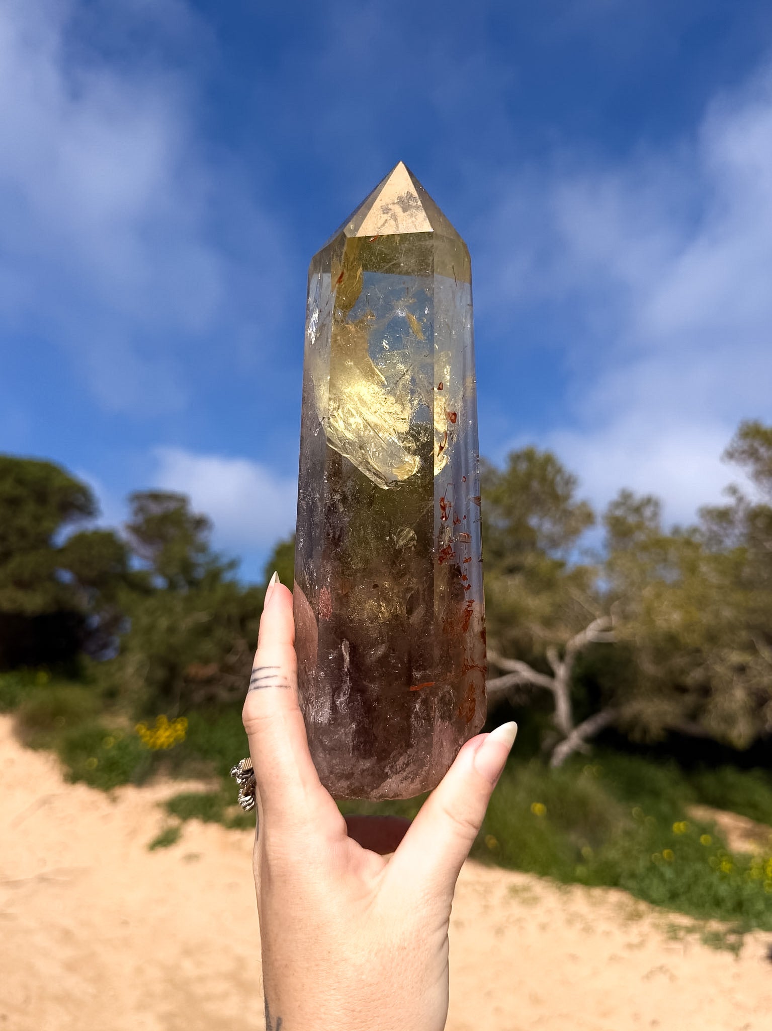 Hand holding large golden brazilian citrine point with a natural background and blue sky 