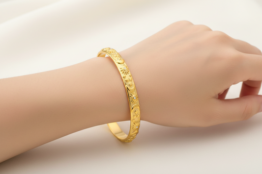 womans wrist wearing Gold bracelet with engraved design on a white background