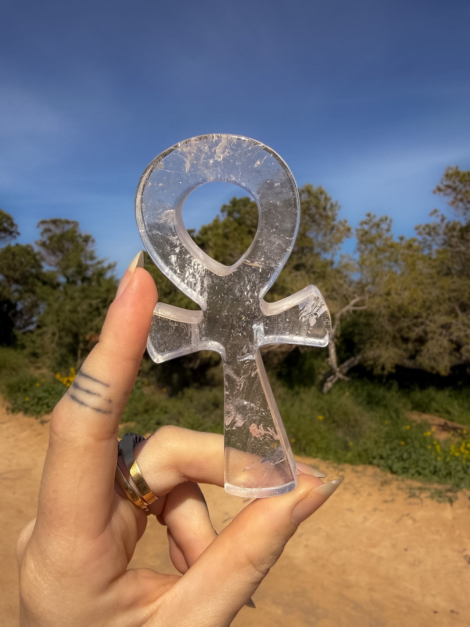 Clear quartz crystal ankh carving held by a hand with a natural landscape background