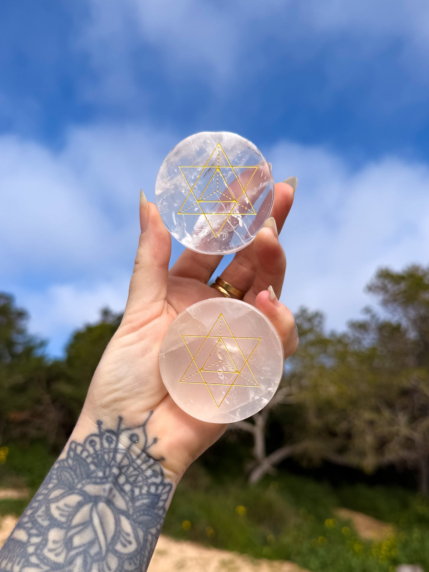 Hand holding two crystal discs with merkaba sacred geometry gold design against a natural background
