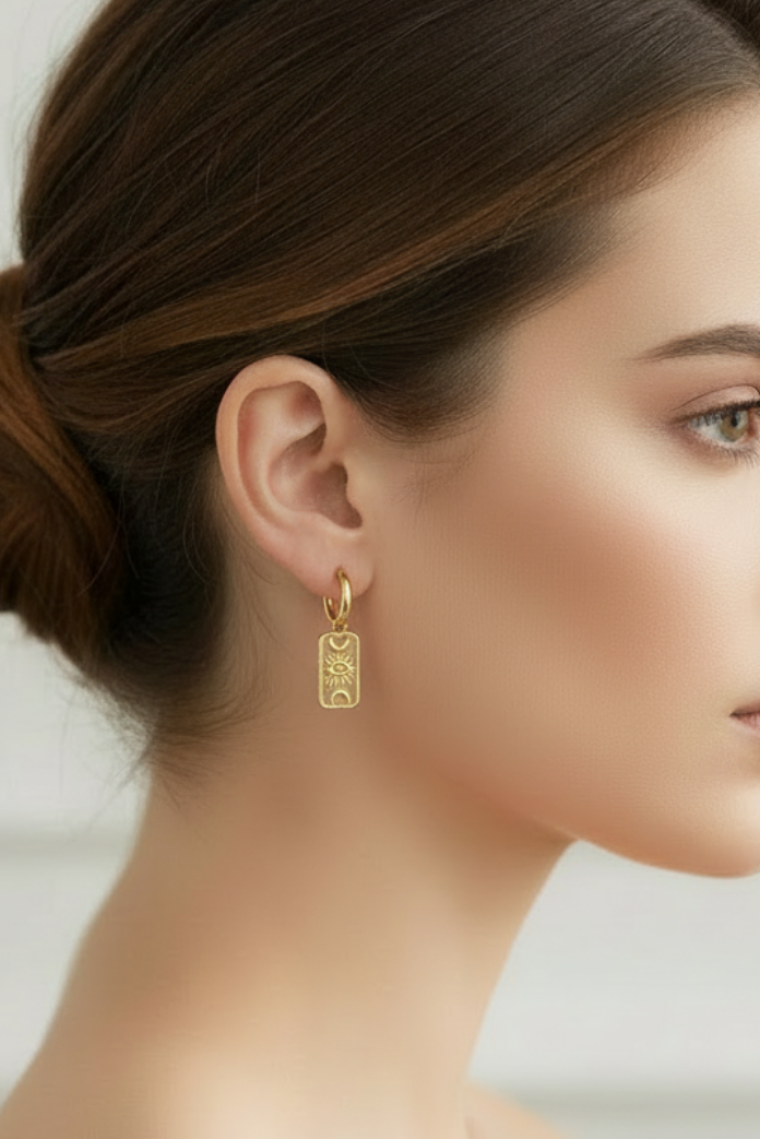 Gold moon and eye long plaque huggies earrings with on womans side profile with brown hair and white background