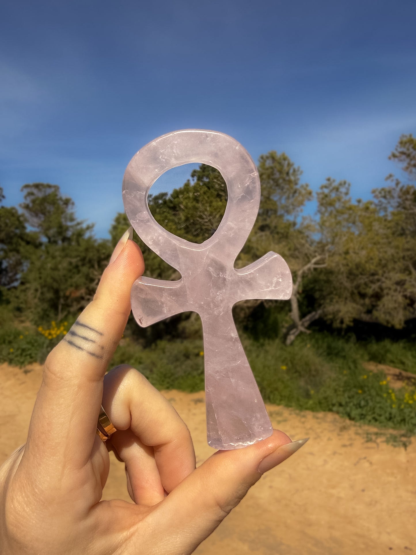 rose quartz crystal ankh carving held by a hand with a natural landscape background