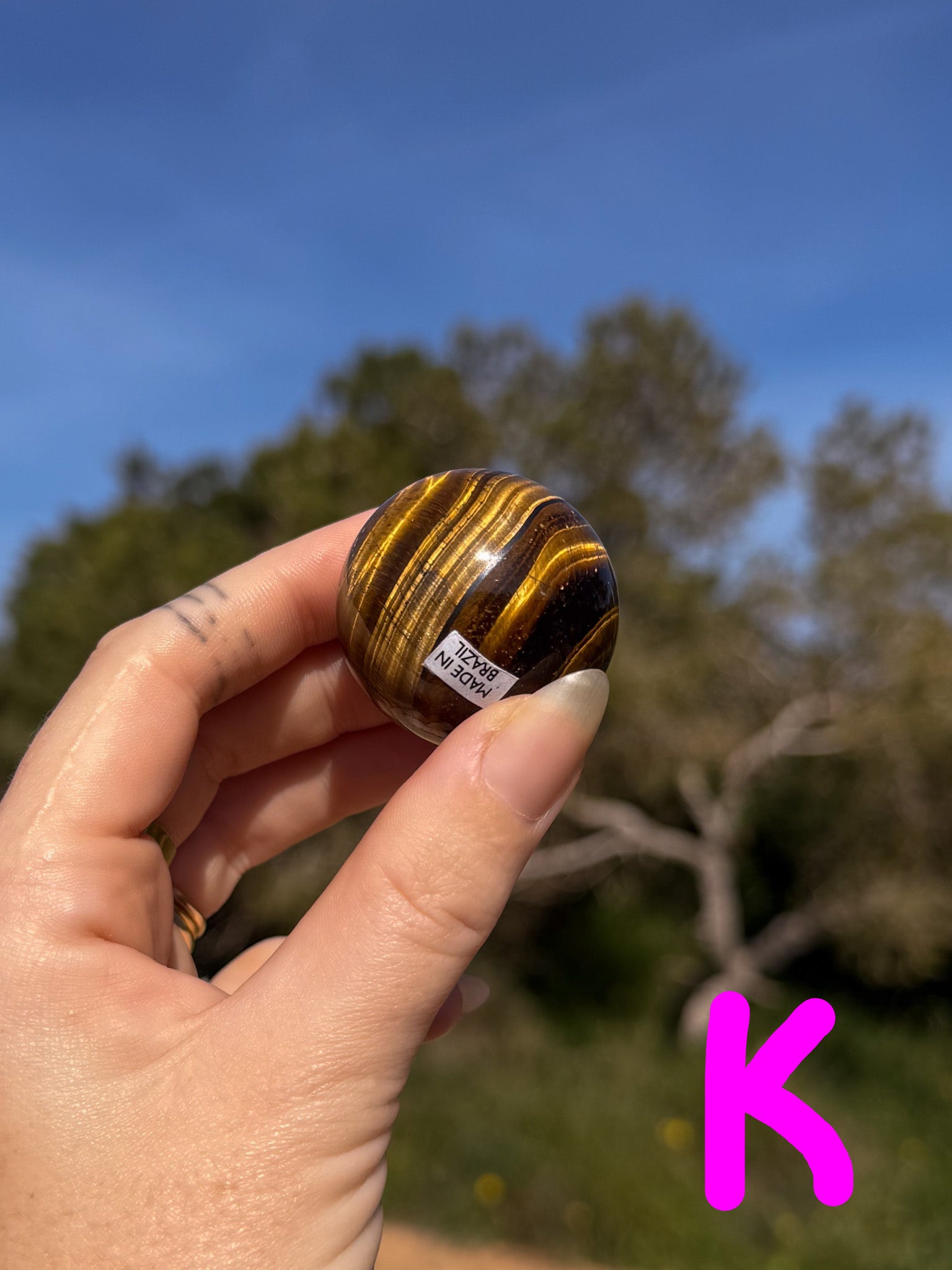 Hand holding a small tiger's eye crystal sphere with a blurred natural background