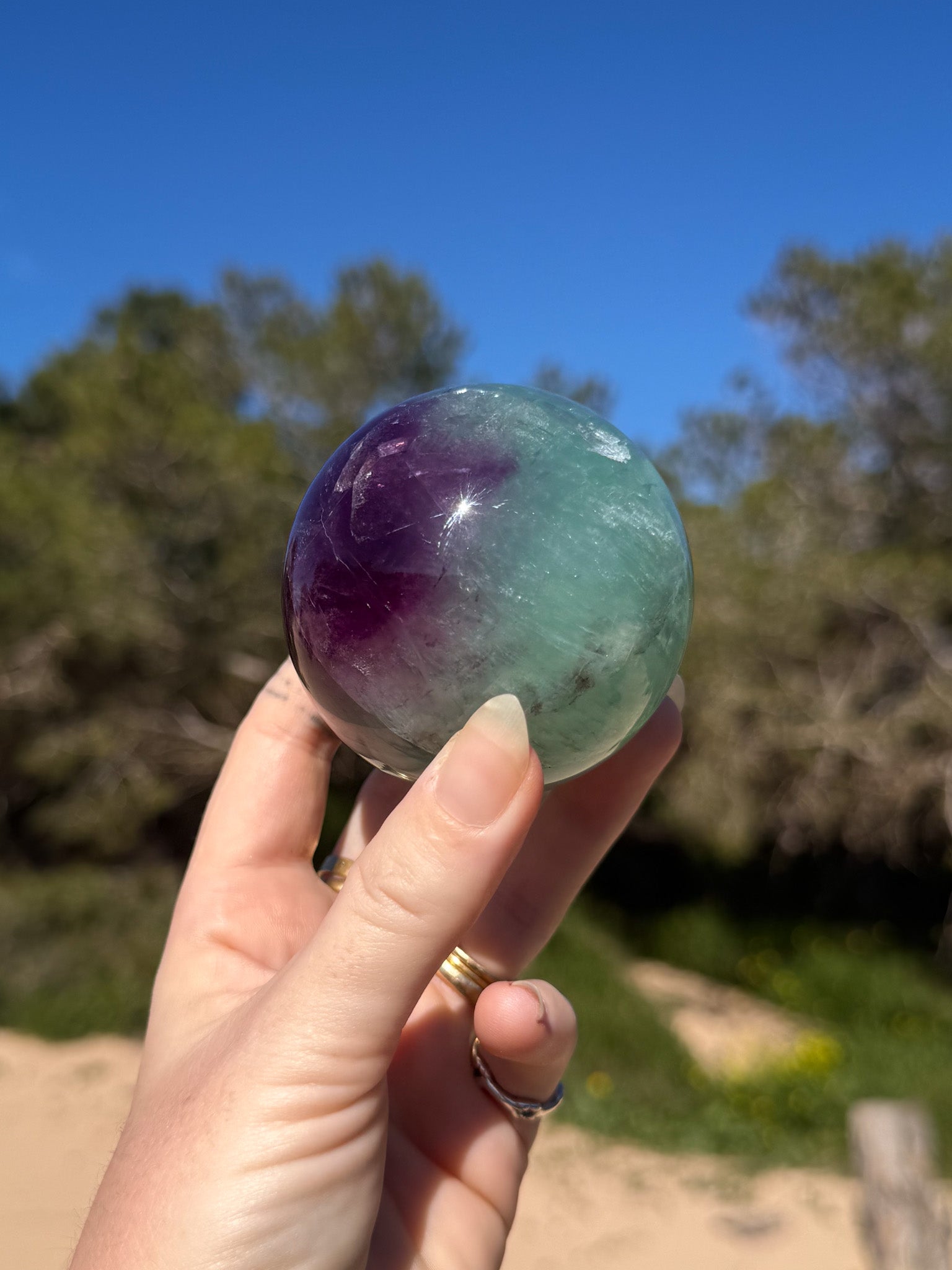 hand holding vibrant green and purple crystal sphere with green and sandy natural background