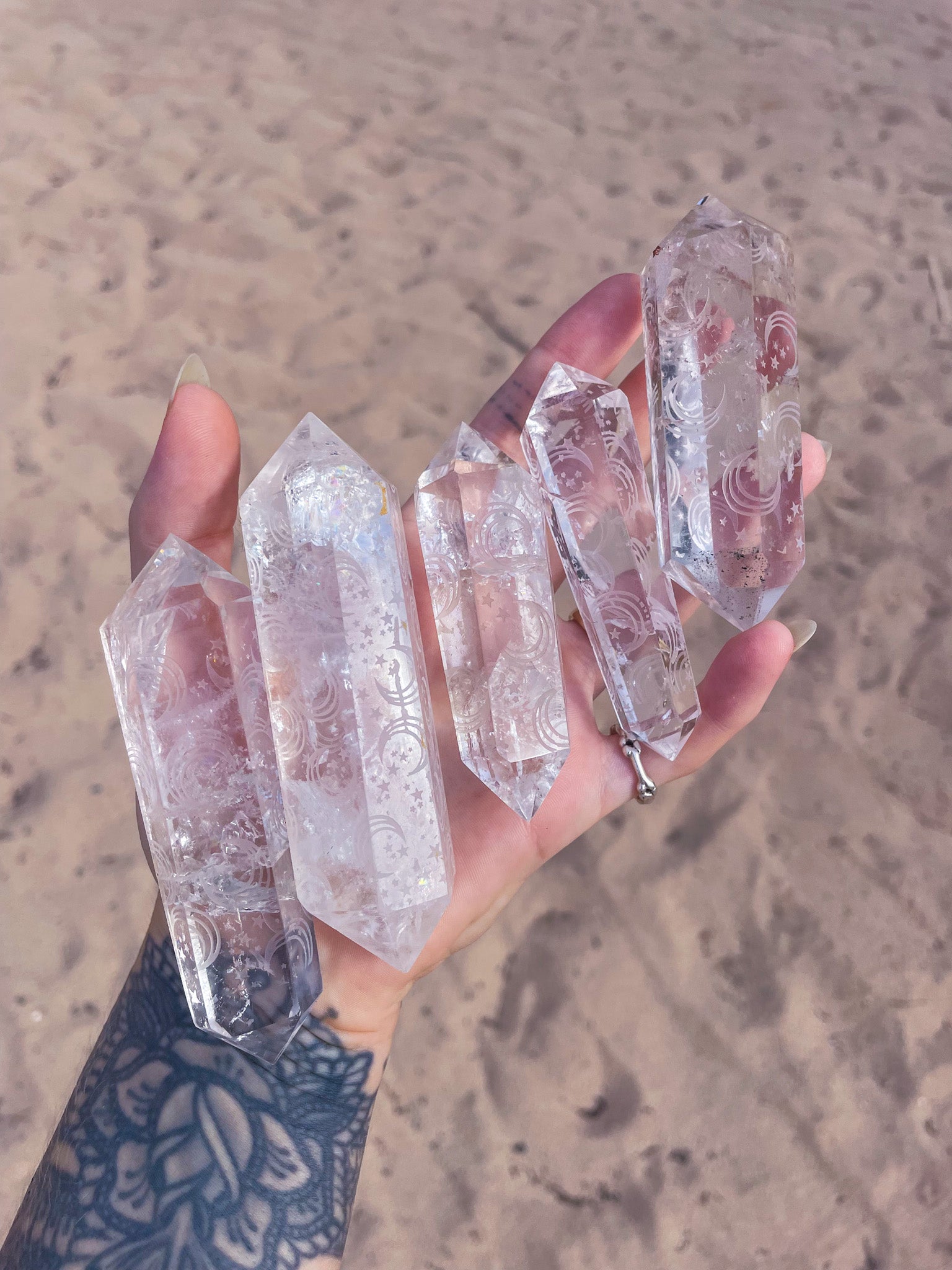 hand holding several laser printed DT clear quartz points with sun stars and moon patterns on the crystals over a sandy background