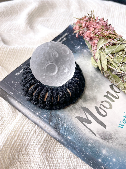 full quartz moon sat on black macrame stand on a moon rituals book and herb smoke bundle 